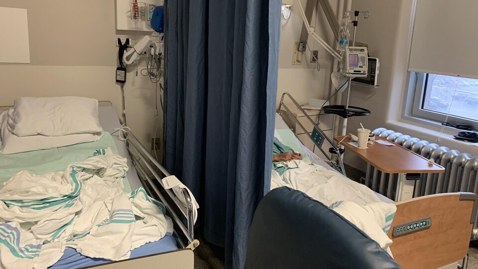 Deux lits d'hôpital séparés par un rideau.
