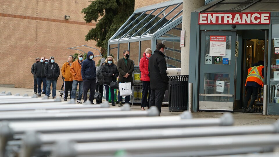 Des habitants de London, en Ontario, font la queue pour entrer dans un supermarché.