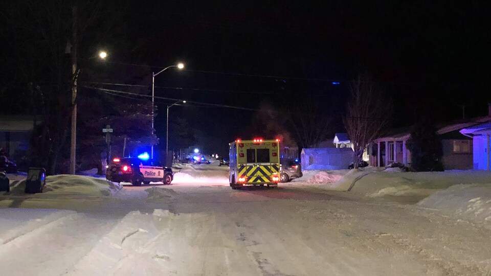 Une voiture de police et une ambulance dans une rue enneigée le soir.