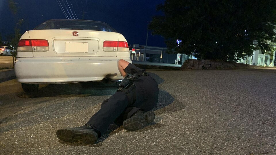Un policier couché par terre en train de regarder sous une voiture modifiée