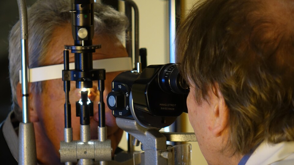 Un médecin examine l'oeil d'un patient à travers un appareil d'ophtalmologie.