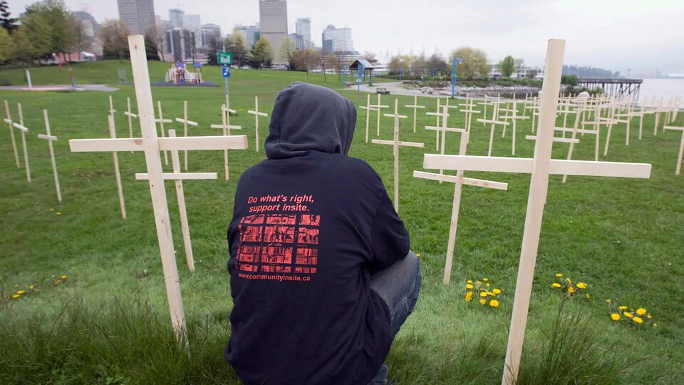 Un homme accroupi devant plus de 1000 croix plantées pour illustrer le nombre de vies sauvées par le site d'injection supervisé de Vancouver.