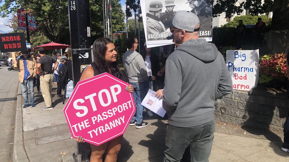 Deux personnes parlent ensemble, l'une d'entre elles tient une pancarte où il est écrit, en anglais, « Stop à la tyrannie du passeport ».