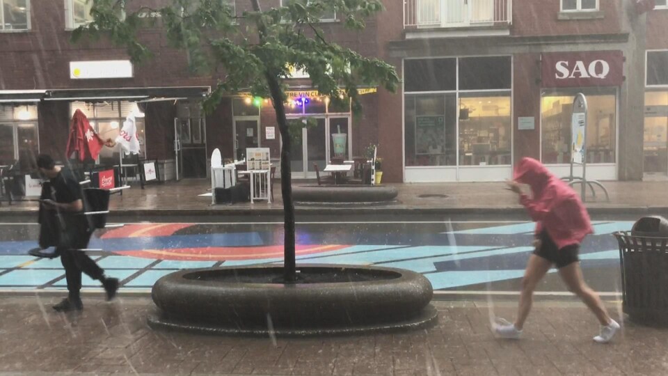 Deux personnes avancent avec difficulté sous la pluie au centre-ville de Trois-Rivières.