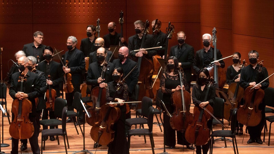 Des musiciens et musiciennes debout avec leurs instruments à cordes dans une salle de concert.