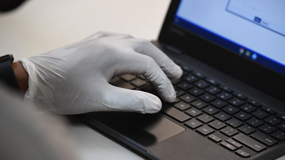 Une personne portant des gants de plastique utilise un ordinateur portable.