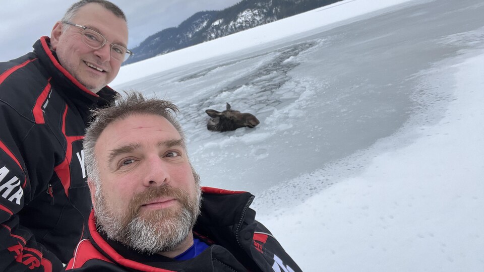 Shawn Duquette et son ami André Roberge debout sur un lac gelé devant une orignale immergée