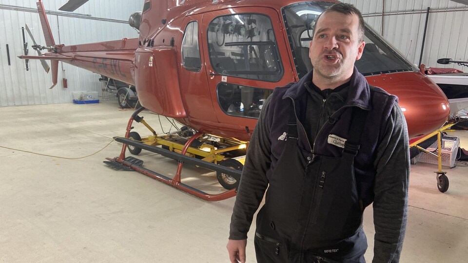 Jean-François Plourde parle devant un hélicoptère dans un hangar.