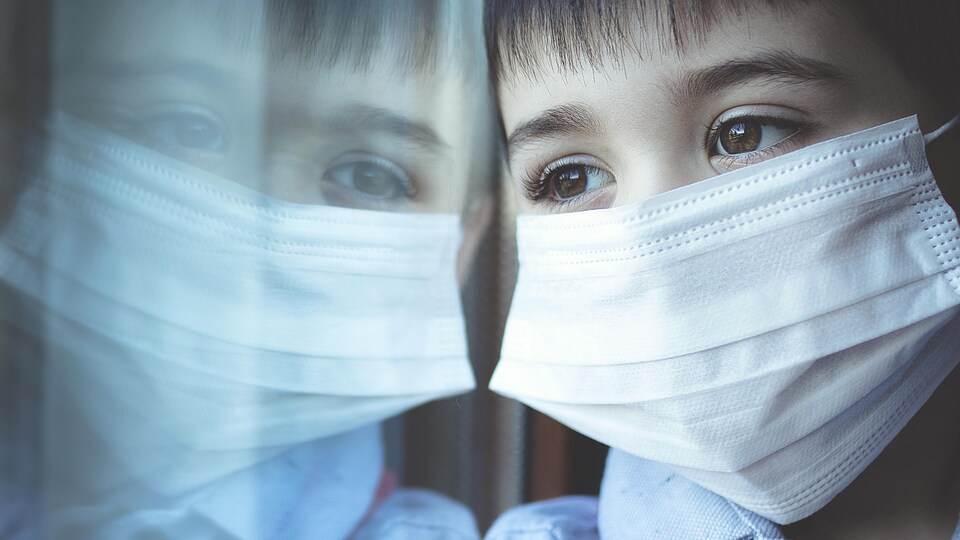 Un jeune garçon masqué regardant son reflet dans une vitre.