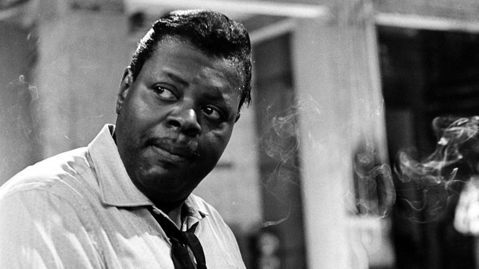 Oscar Peterson, les mains sur le clavier d'un piano, regardant au loin.