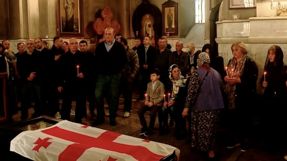 A crowd gathered around a coffin wrapped in the Georgia flag in a church.