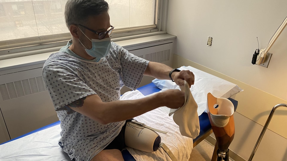 Assis sur un lit d'hôpital, Pierre Marinier tient la chaussette qui fait partie de l'emboîture de sa prothèse.