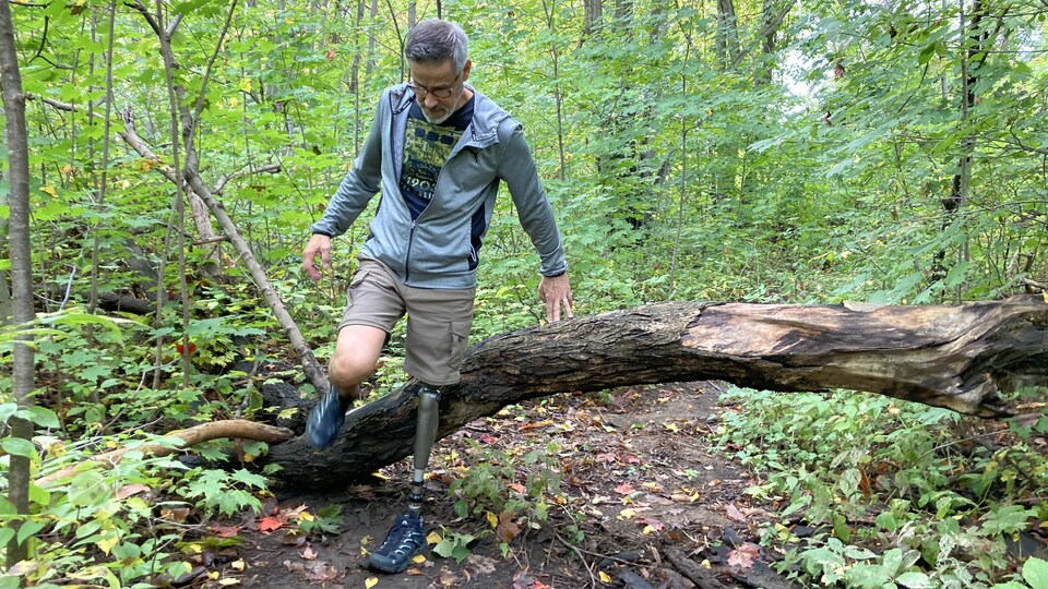 En forêt, Pierre Marinier enjambe avec son membre artificiel un tronc d'arbre couché au sol.
