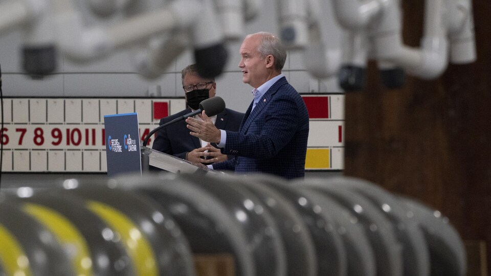 M. O'Toole, de profil, parle aux journalistes en point de presse. Au premier plan, des pierres de curling. En arrière-plan, le décor d'une salle de curling.