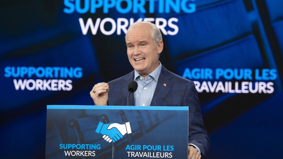 On voit M. O'Toole qui s'adresse aux aux journalistes, de face. Derrière lui, le slogan du Parti conservateur "Supporting workers" ou "Agir pour les travailleurs".