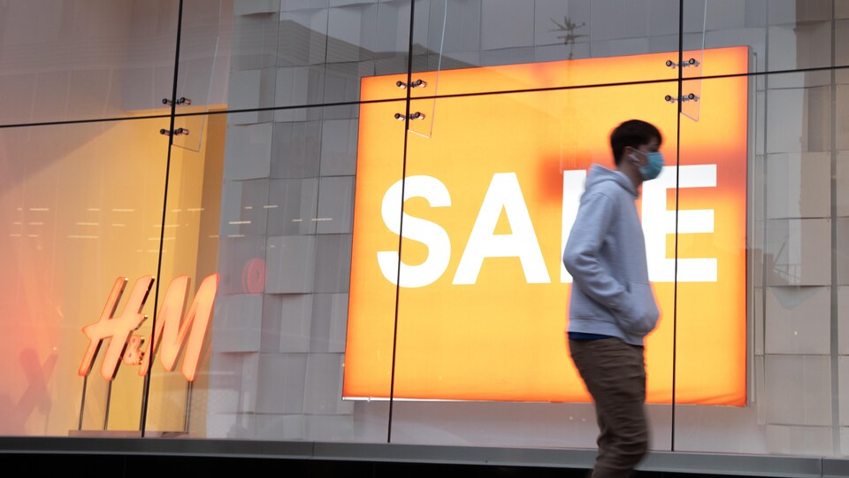 Un homme masqué marche devant la vitrine d'un magasin H&M.