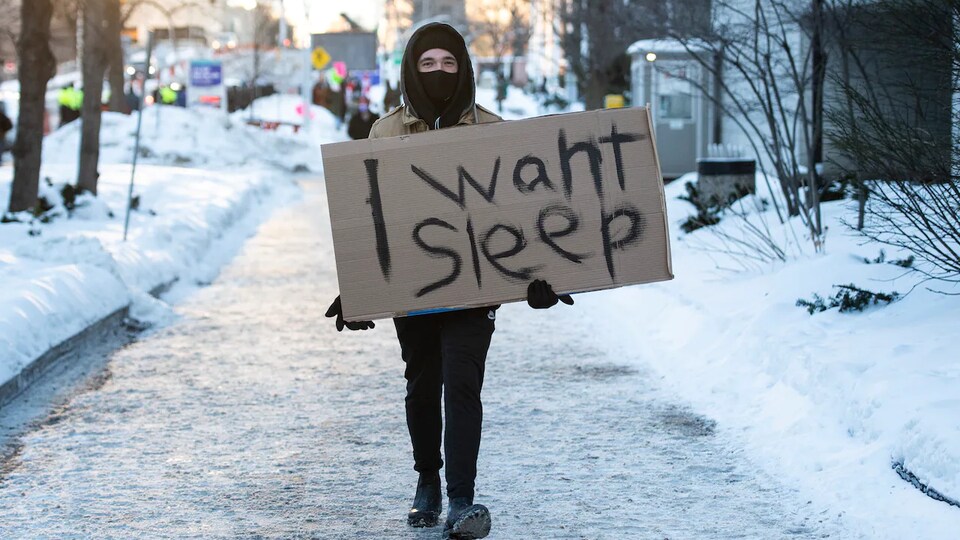 Un homme tient une pancarte où il est écrit, en anglais : Je veux dormir.