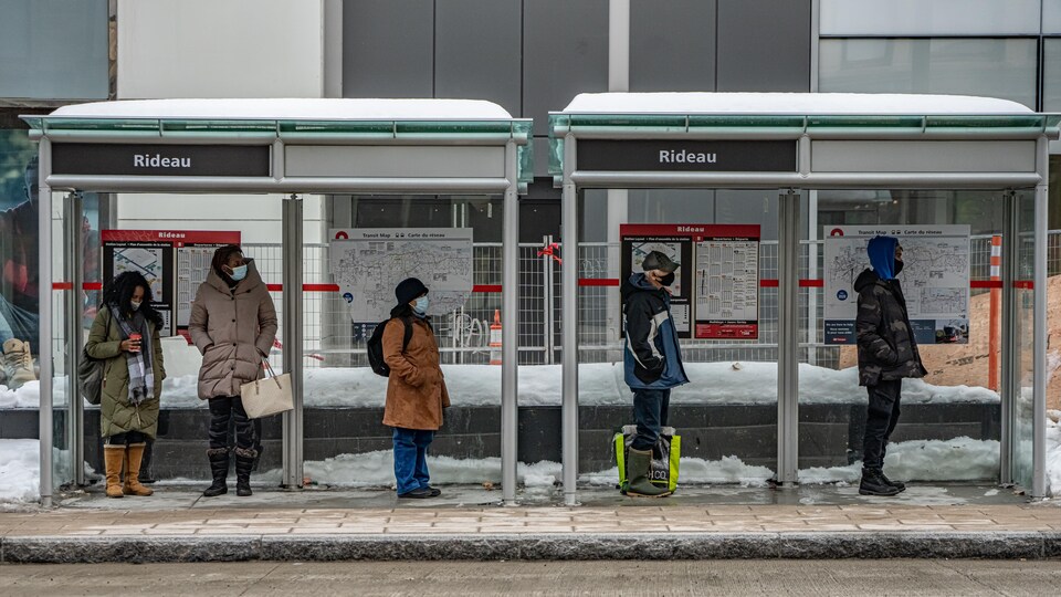 Des gens portant un masque attendent l'autobus.