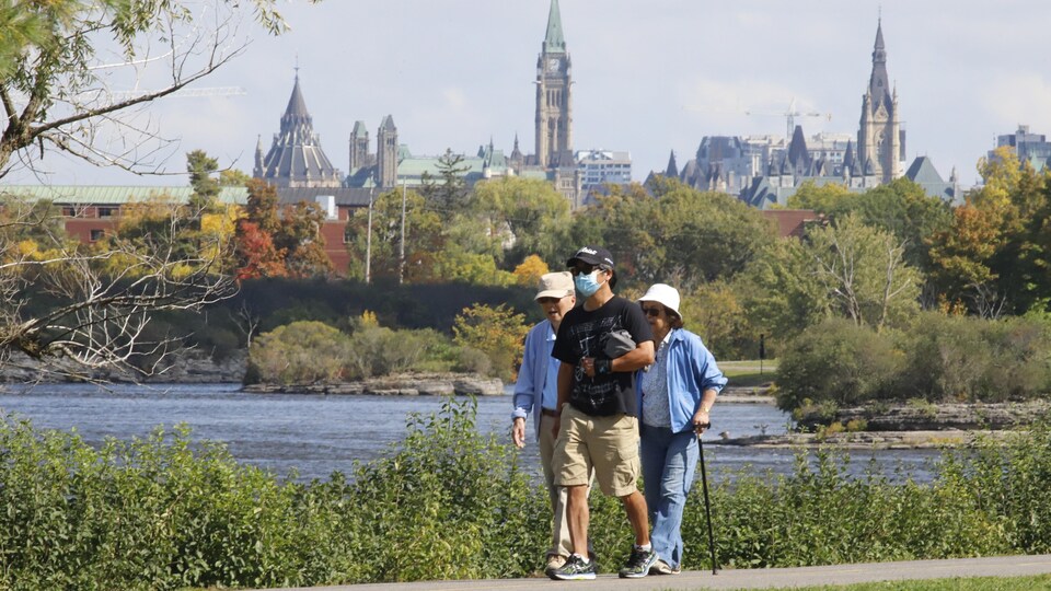 Deux hommes et une femme marchent près du Parlement du Canada.