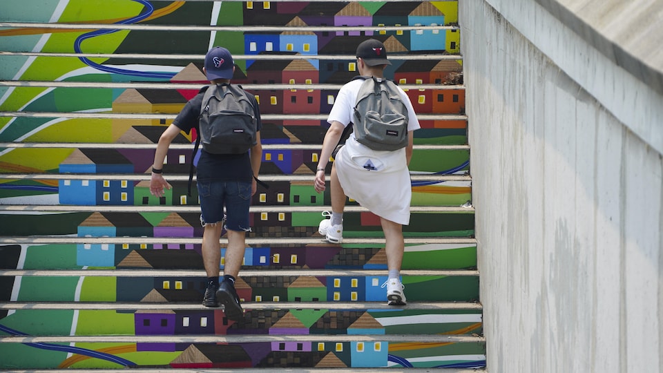 Deux garçons de dos grimpent les marches peintes en murale.