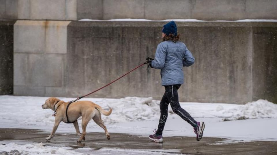 Une femme court en tenant son chien en laisse.