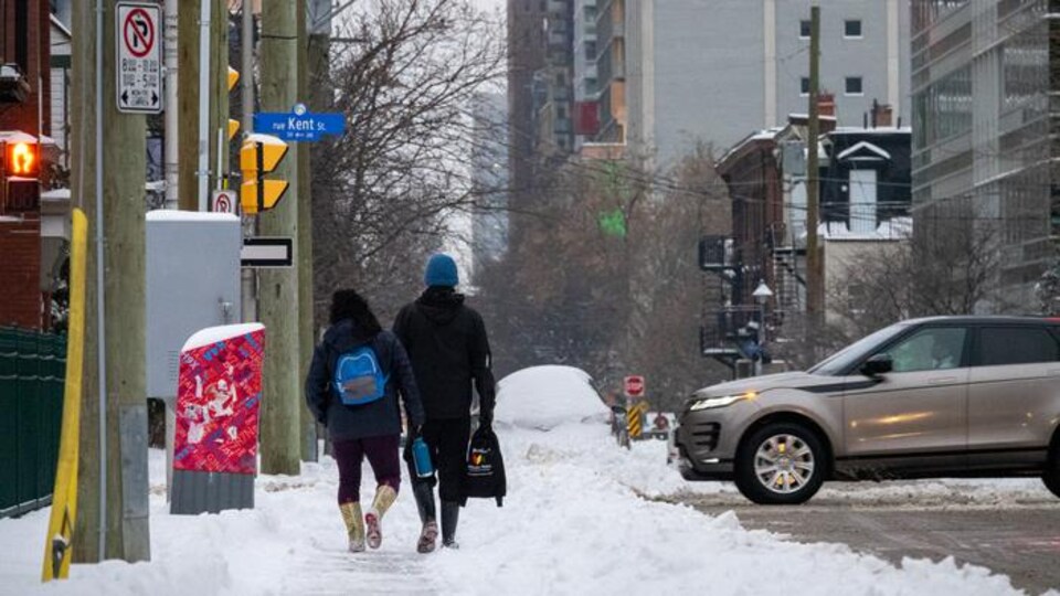 Deux piétons marchent sur le trottoir enneigé de la rue Kent à Ottawa.