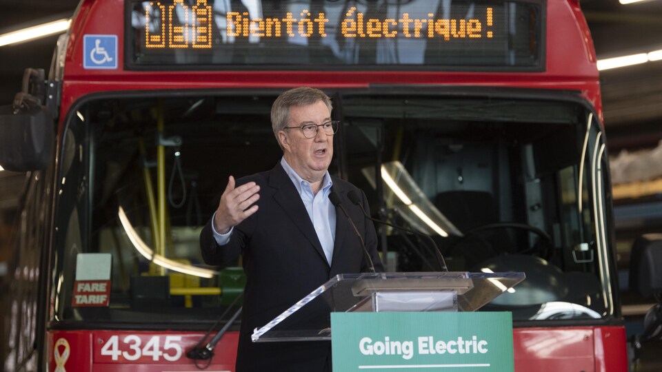 Un homme devant un autobus électrique parle à un micro.
