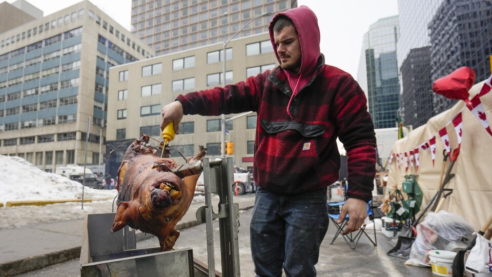 Un homme arrose un porc qui cuit sur une broche dans une rue.