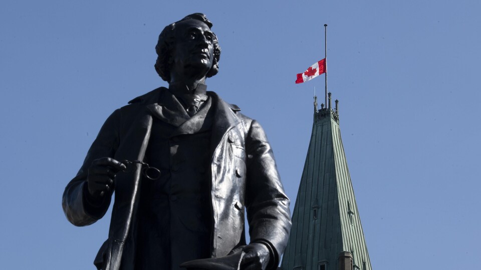 Le drapeau canadien est en berne au-dessus de la tour de la Paix, près d'une statue, sur la colline du Parlement à Ottawa.