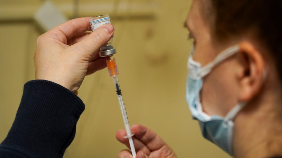 Un homme dans un centre de vaccination à Ottawa remplit une seringue.