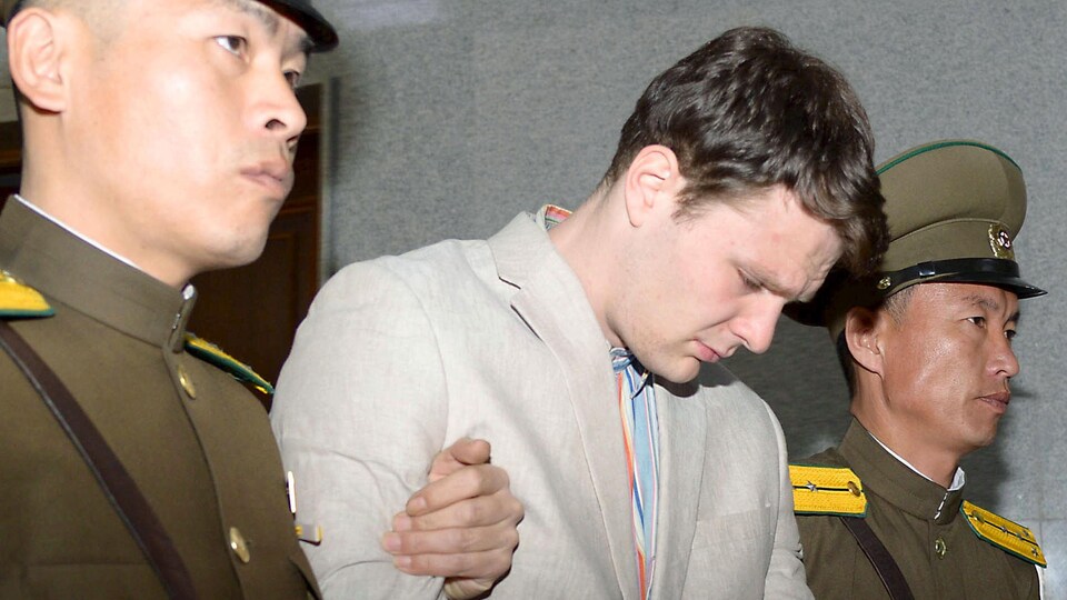 Un jeune homme la tête baissée, entre deux policiers nord-coréens
