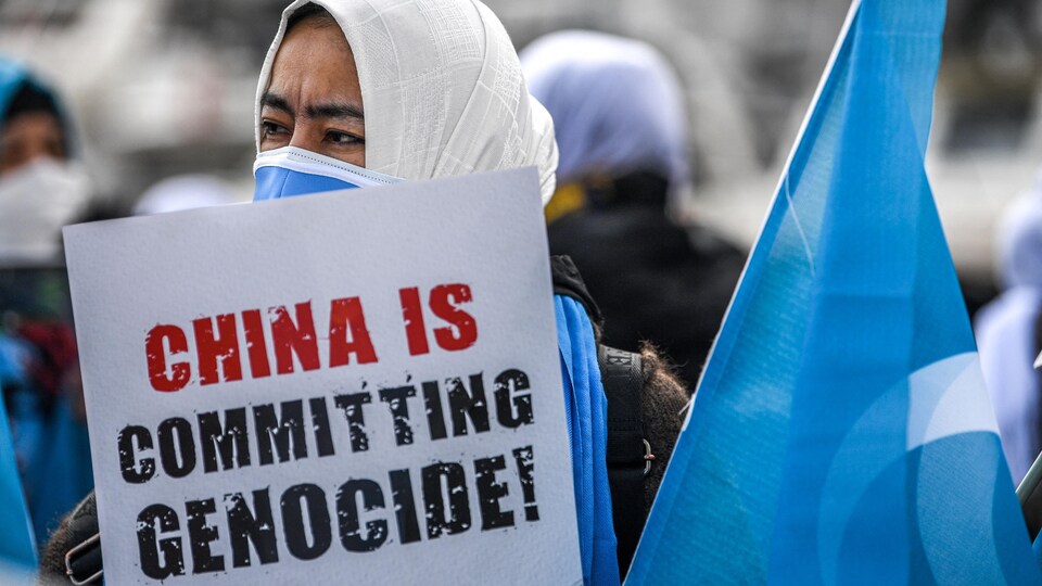 Une femme tient une affiche dénonçant le « génocide des Ouïgours ».