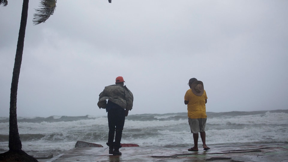 Deux hommes sont debout sur une plage devant la mer déchaînée.