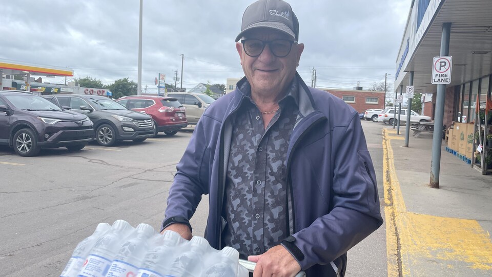 Un homme pousse un panier d'épicerie rempli de bouteilles d'eau.