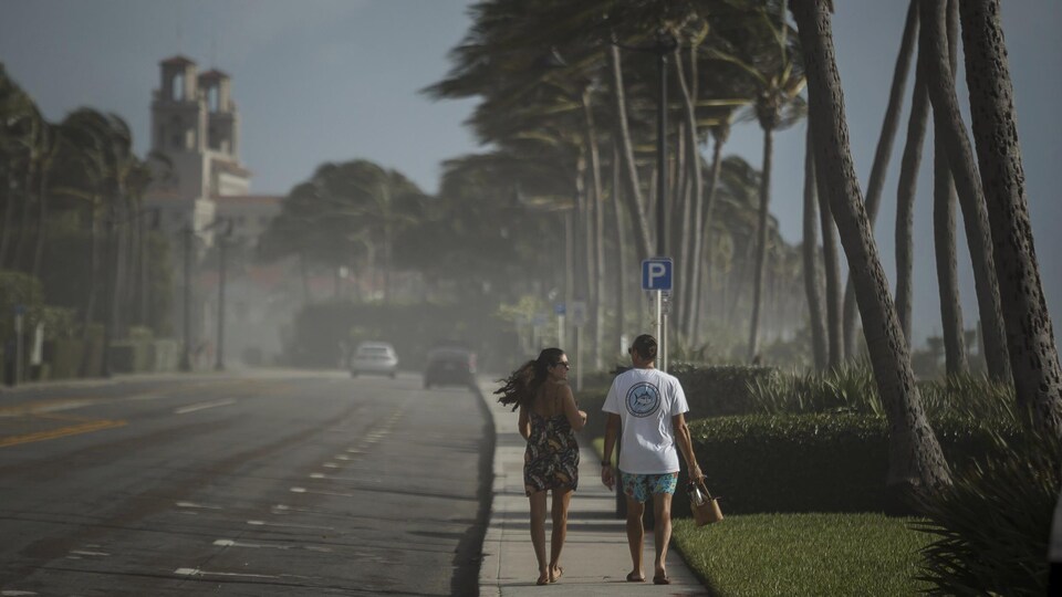 Un couple marche sur un trottoir sous un fort vent.
