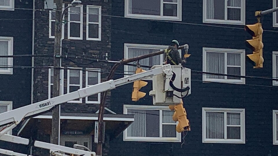 Un pompier dans un escalier en hauteur répare un lampadaire. 