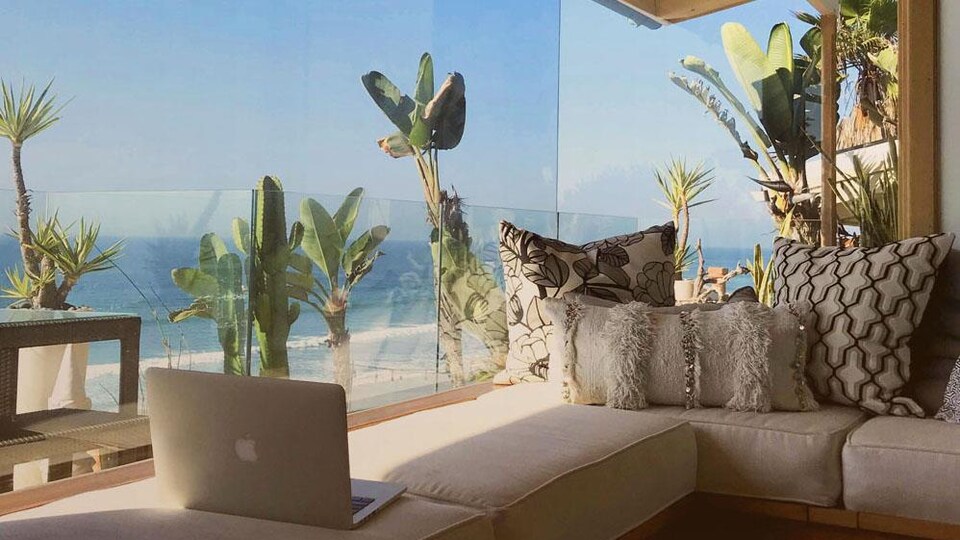 Un ordinateur portable posé sur un sofa près d'une fenêtre avec vue sur la mer.