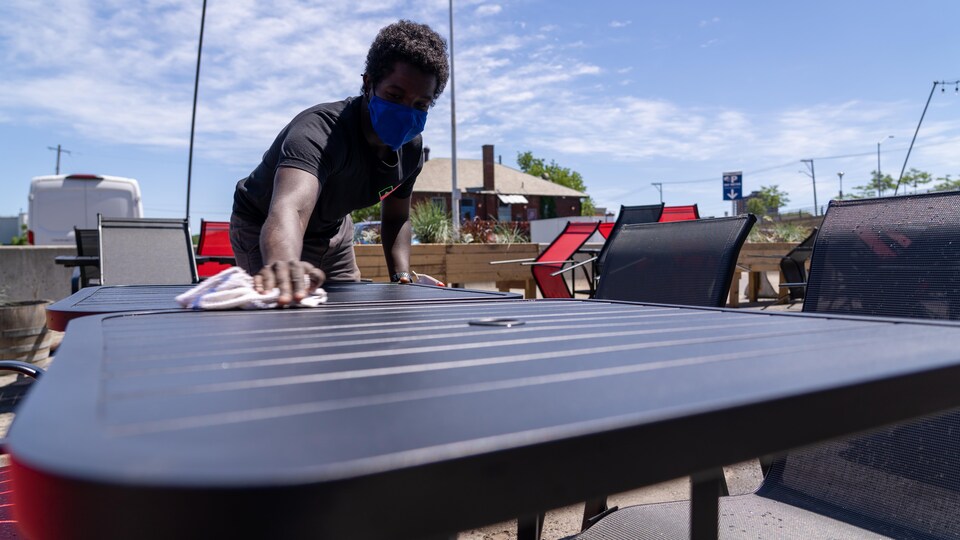 Un employé lave une table sur une terrasse.