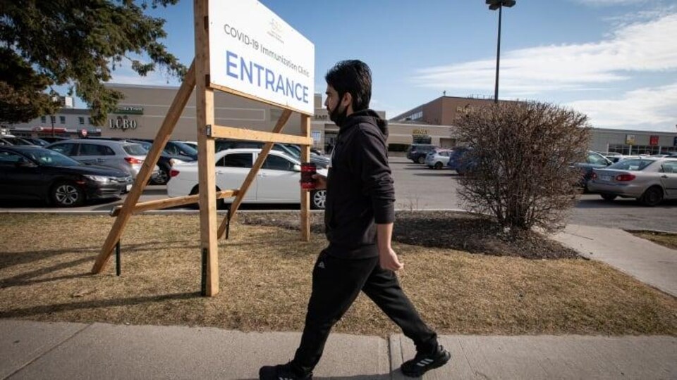 Un homme, tenant un café, marche d'un pas actif sur le trottoir.