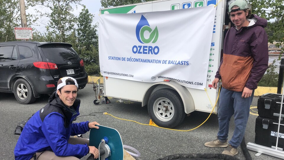 Deux jeunes hommes posent près d'une station de lavage de bateaux, souriants.