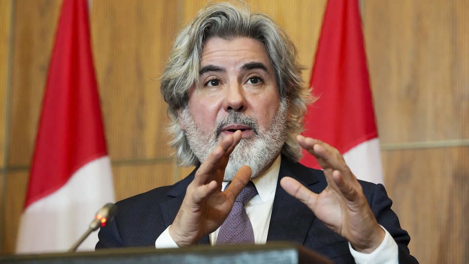 Pablo Rodriguez speaks in front of two Canadian flags.