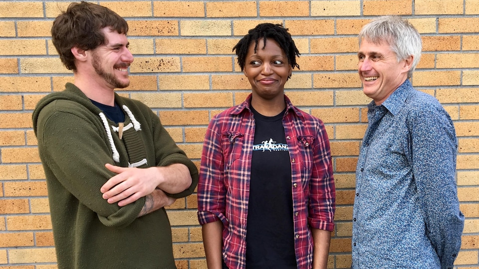 Deux hommes et une femme se tiennent debout devant un mur et se sourient l'un à l'autre.