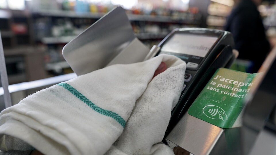 Une main tient un linge et nettoie une machine qui sert à payer avec une carte de crédit ou de débit.