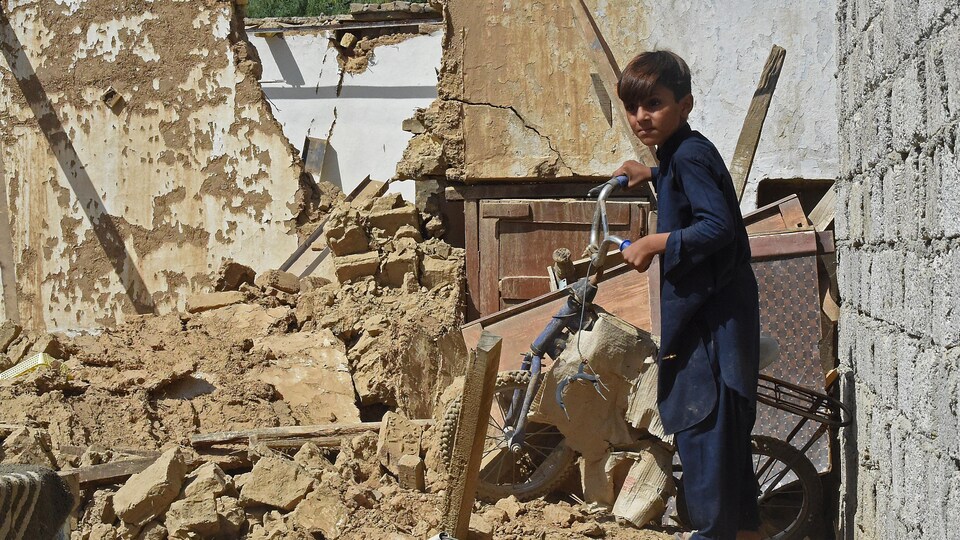 Un garçon tient un vélo endommagé dans les ruines d'une maison.