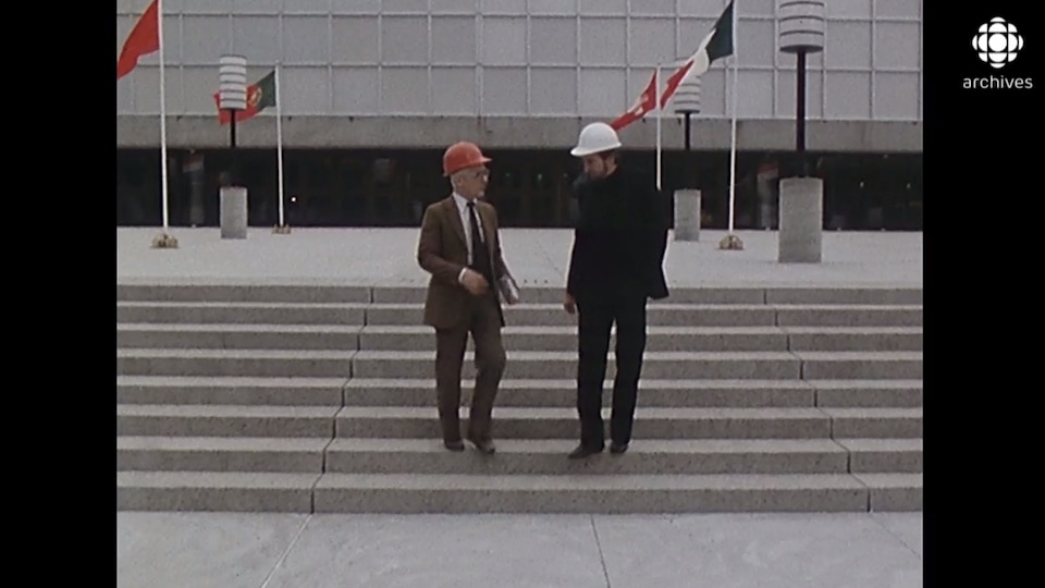 Deux hommes portant un casque de construction descendent les marches du bâtiment. 