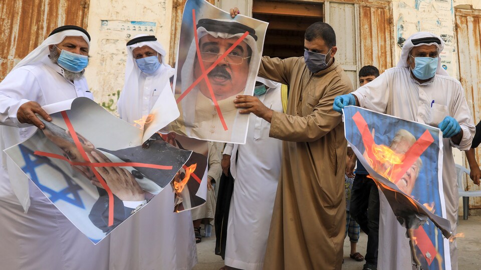 Des hommes avec des masques contre la COVID-19 tiennent des affiches en feu représentant les trois hommes d'État.