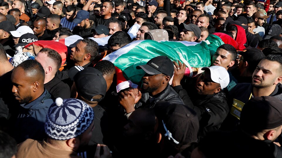 Une foule transporte des corps enveloppés dans des drapeaux palestiniens.