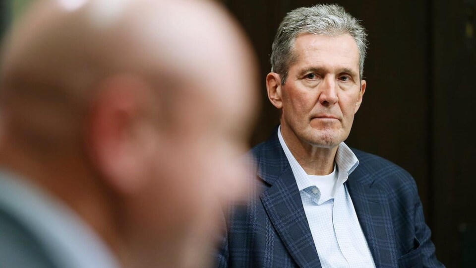 Le premier ministre Brian Pallister, vu de face, regarde Brent Roussin qui est au premier plan sur la photo, et dont le visage de profil est hors focus.