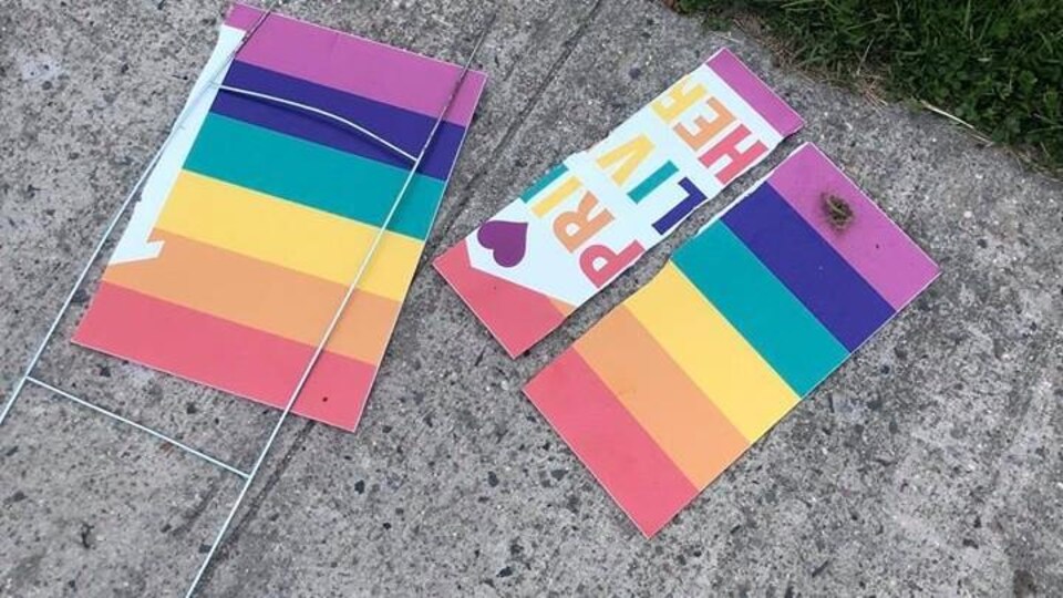 Un panneau aux couleurs du drapeau de la Fierté repose en trois morceaux sur une dalle de béton.