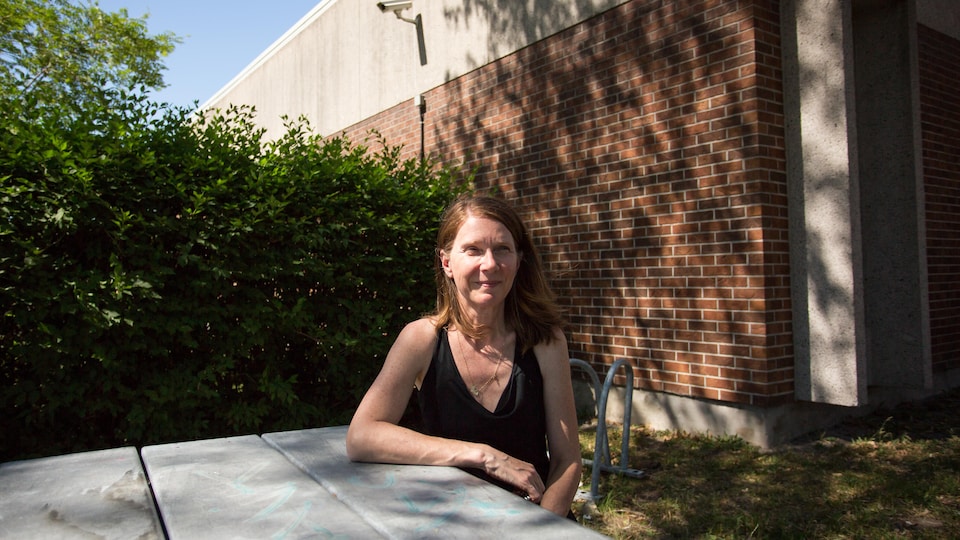 Guylaine Beaubien est assise à une table devant l'école où elle enseigne.